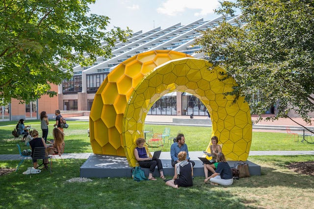 Students sit around a yellow grid structure by Andres Svetsuk oustide of Gund Hall.